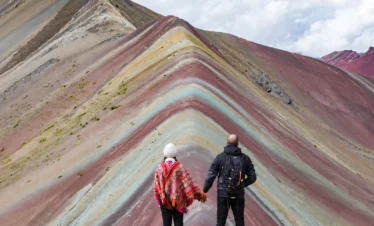 Couple holding hands while facing the colorful mineral bands of Rainbow Mountain, Peru.