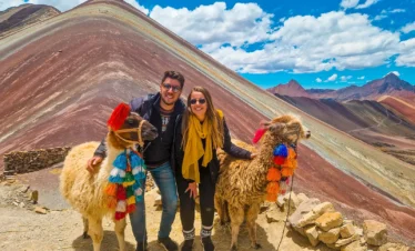 Couple posing with two decorated llamas beside the colorful slopes of Rainbow