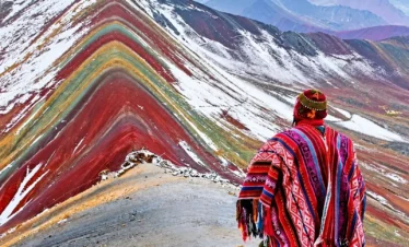 Traveler wearing a red Andean poncho overlooking the colorful, snow-dusted slopes of Rainbow Mountain.