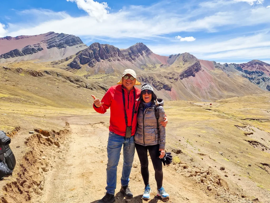 Two travelers posing on a mountain trail surrounded by rugged Andean peaks near Rainbow Mountain.llamas beside the colorful slopes of Rainbow Mountain, Peru.