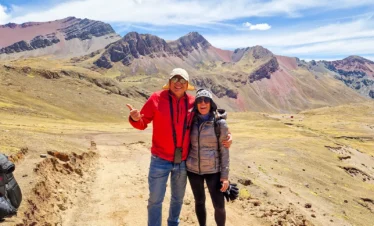 Two travelers posing on a mountain trail surrounded by rugged Andean peaks near Rainbow Mountain.llamas beside the colorful slopes of Rainbow Mountain, Peru.