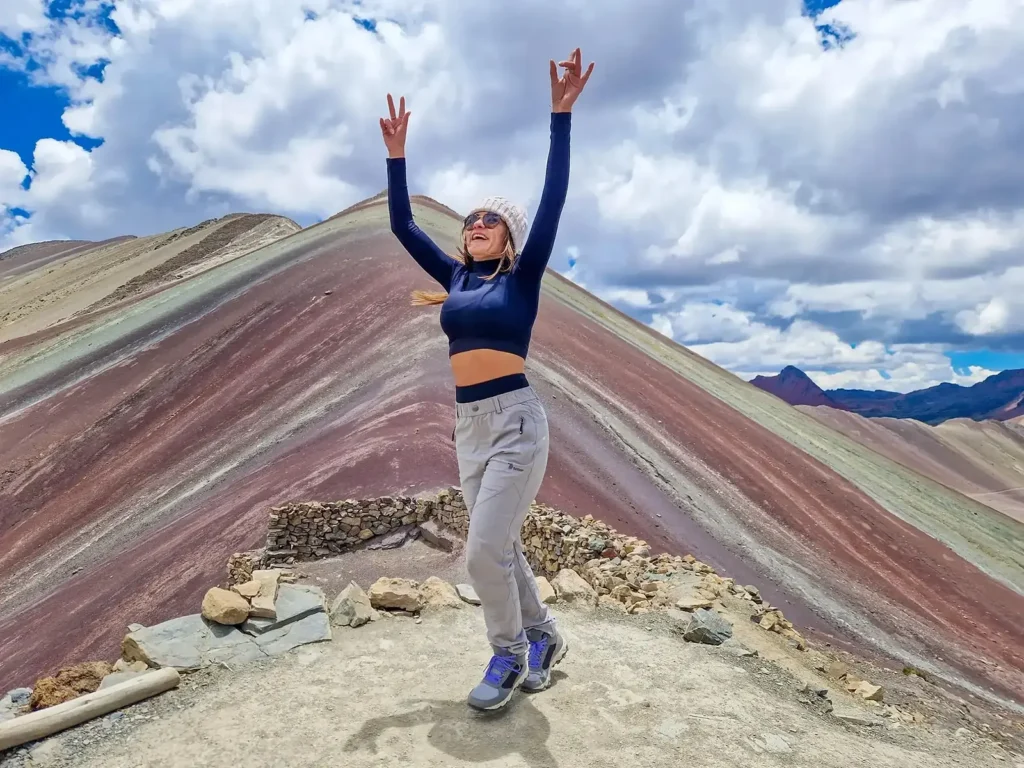 Woman raising her arms at a viewpoint overlooking Rainbow Mountain in Cusco, Peru.