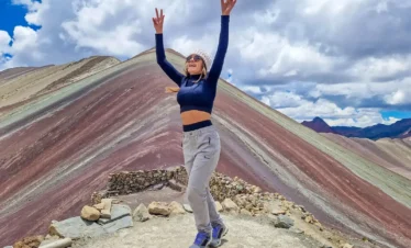 Woman raising her arms at a viewpoint overlooking Rainbow Mountain in Cusco, Peru.