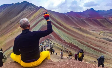 Traveler in yellow pants overlooking Rainbow Mountain and hikers at the viewpoint in Cusco, Peru.